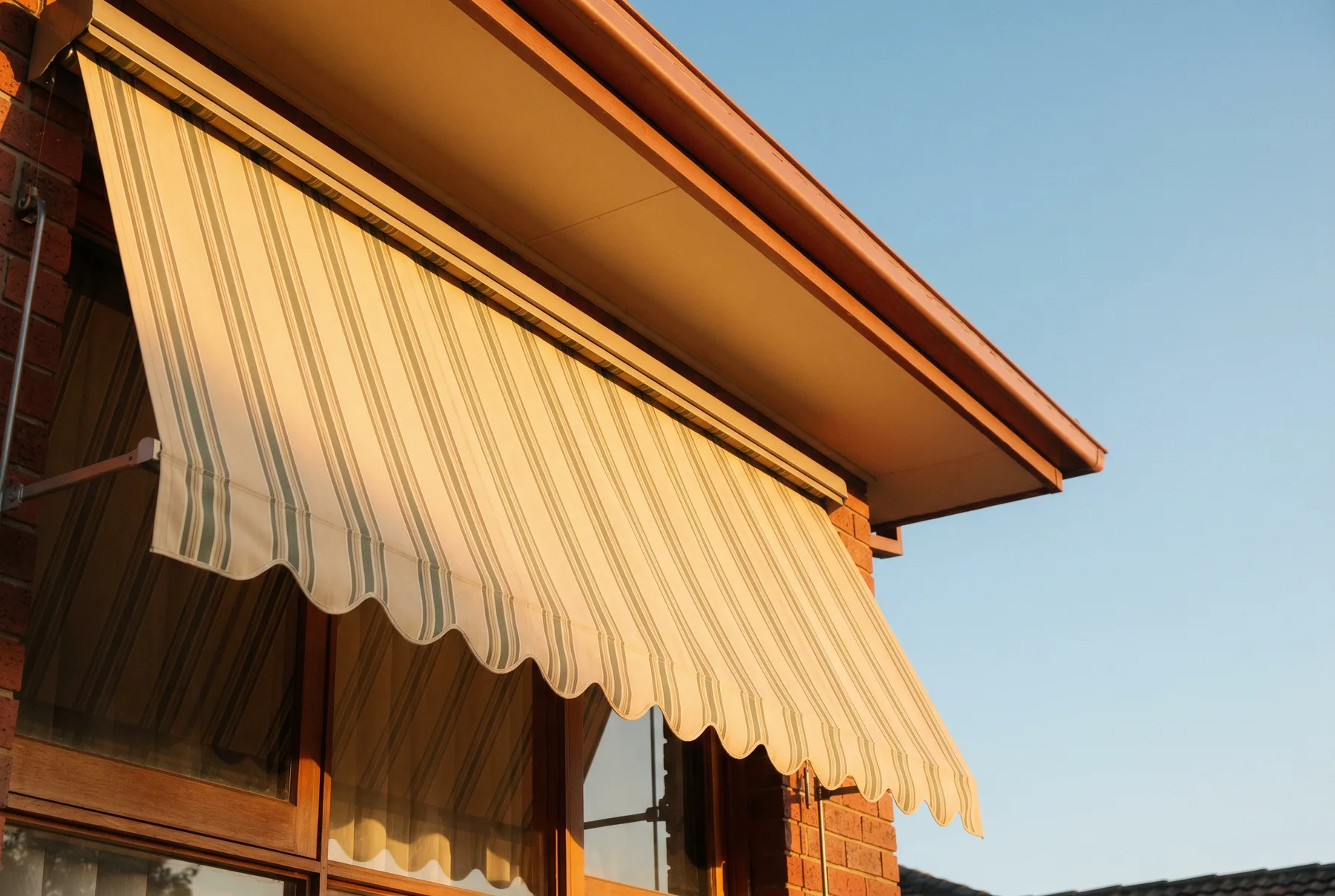 Looking up at a striped canvas awning with a scalloped edge against afternoon sky