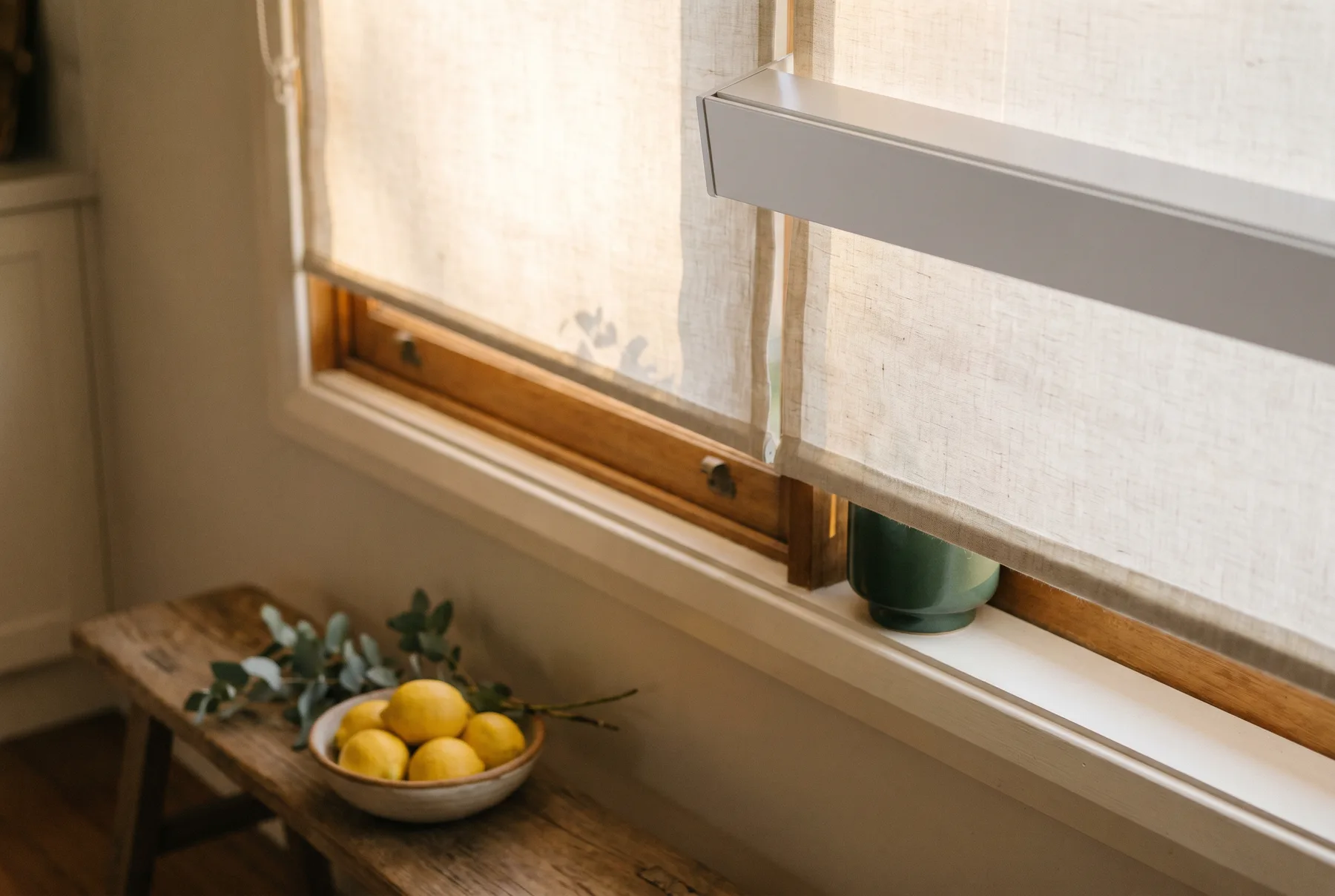 A white roller blind half lowered over a bright kitchen window
